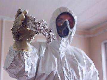 Fachmann in Schutzkleidung und Gesichtsmaske hält ein Stück Asbest hoch